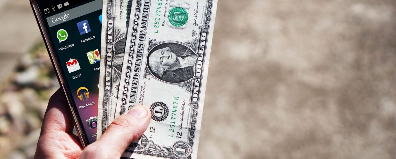 Hand holding smartphone and dollar bills representing withdrawing money from Crypto.com