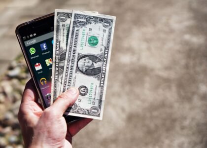 Hand holding smartphone and dollar bills representing withdrawing money from Crypto.com